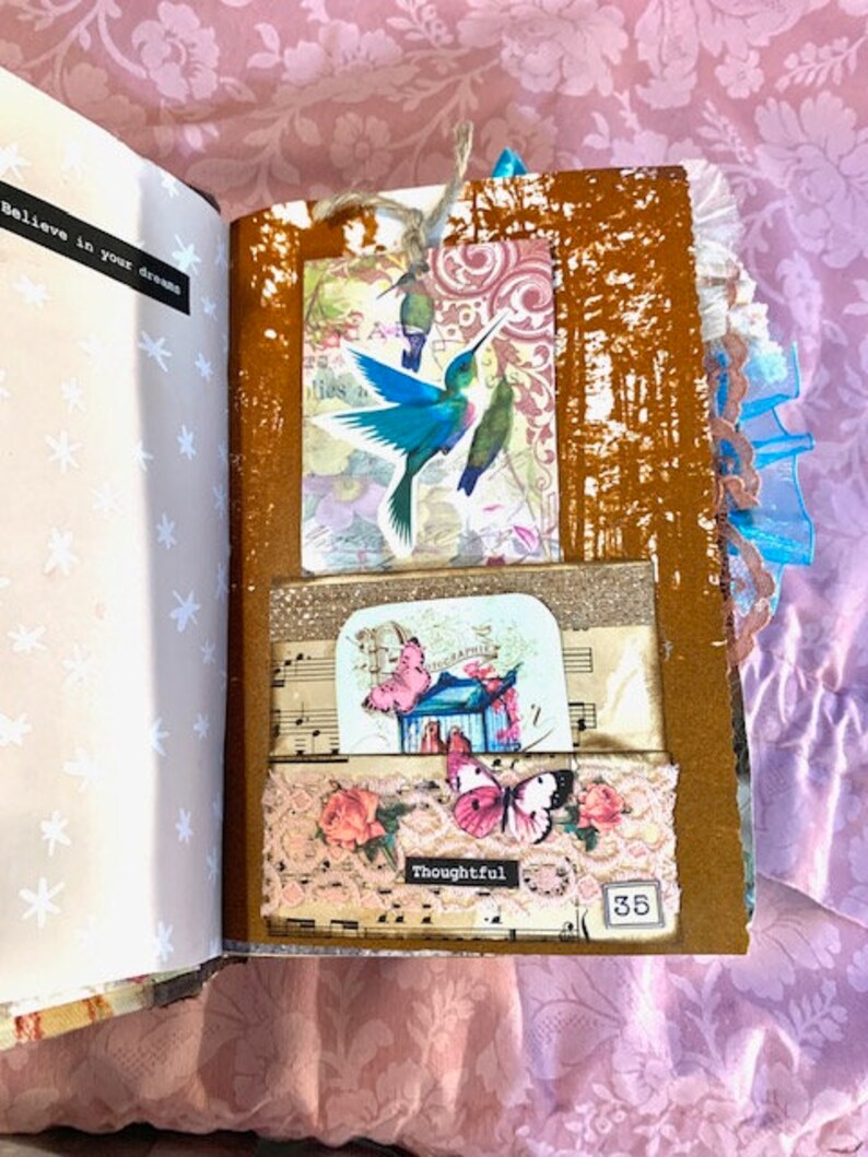 May include: Open journal with decorative pages. Features a hummingbird tag, butterfly and floral embellishments, and the word "Thoughtful". The journal's pages are adorned with musical notes and a "35" tag.