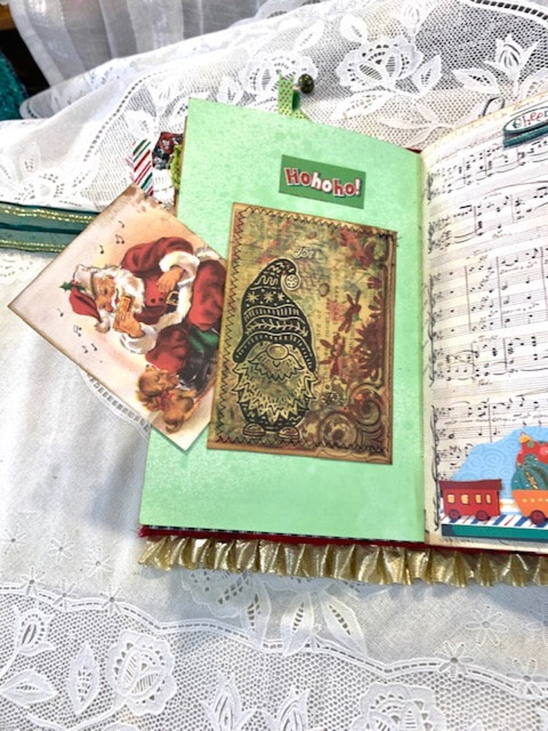 May include: A handmade Christmas journal with a green cover and a decorative gnome image. The journal features a Santa Claus card and the text "Hohoho!" on the cover. The pages have musical notes and a train illustration.