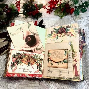 May include: Open journal with Christmas-themed pages. Features include a card with gold bells and the text "Christmas Greetings", a card with a candy cane and ornament, and a card with the text "Merry Christmas". Decorated with holly and ribbons.