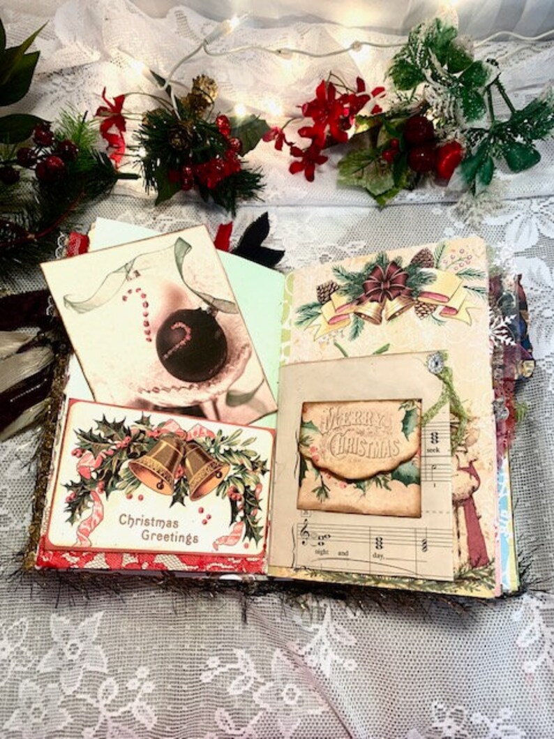 May include: Open journal with Christmas-themed pages. Features include a card with gold bells and the text "Christmas Greetings", a card with a candy cane and ornament, and a card with the text "Merry Christmas". Decorated with holly and ribbons.