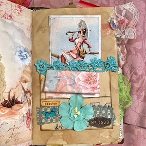 May include: A handmade journal with a vintage aesthetic. Features a collage with a Victorian illustration, teal lace, a paper flower, and the word "passion". The journal has a floral patterned background.