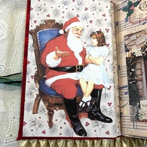 May include: A Christmas-themed journal open to a page with a Santa Claus illustration. Santa, in a red suit and hat, sits in a chair, talking to a girl in a white dress. The page has a white background with a pattern of pine needles and red berries.