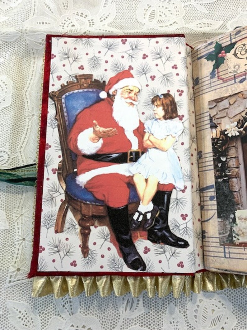 May include: A Christmas-themed journal open to a page with a Santa Claus illustration. Santa, in a red suit and hat, sits in a chair, talking to a girl in a white dress. The page has a white background with a pattern of pine needles and red berries.