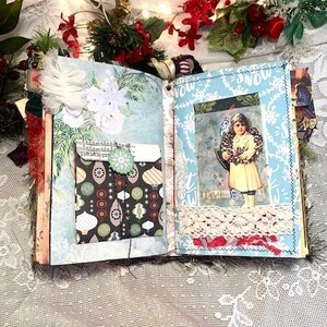 May include: Open journal with Christmas-themed pages. The left page has a pocket with a patterned design and a green button. The right page features a vintage image of a child with a wreath. The journal is decorated with lace and festive embellishments.