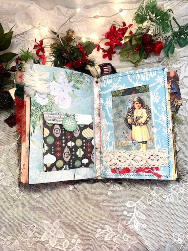 May include: Open journal with Christmas-themed pages. The left page has a pocket with a patterned design and a green button. The right page features a vintage image of a child with a wreath. The journal is decorated with lace and festive embellishments.