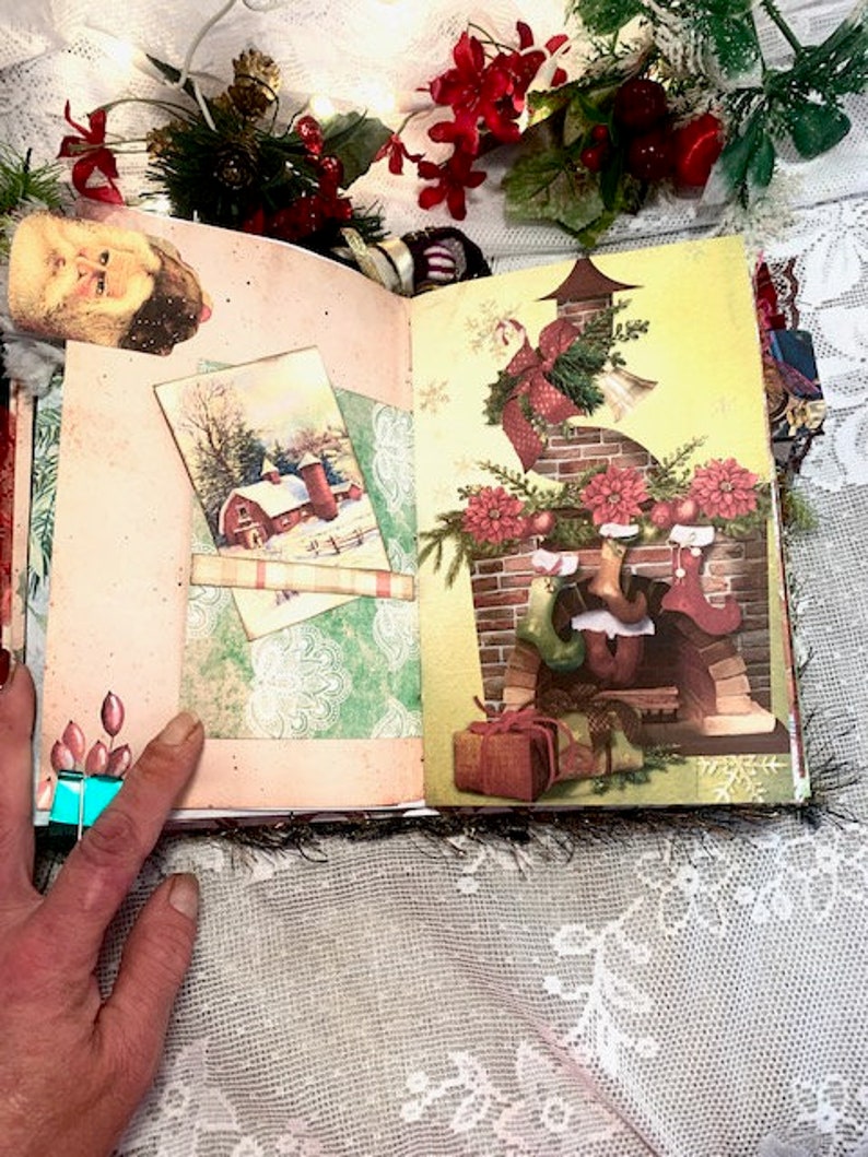 May include: Open journal with Christmas-themed illustrations. One page features a winter scene with a red barn, while the other depicts a decorated fireplace with stockings. The journal is adorned with festive embellishments and a Santa Claus image.