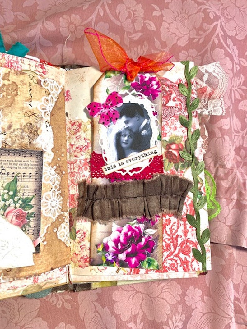 May include: Open scrapbook page with vintage floral and lace elements. Features a black and white photo with the text "this is everything". Embellished with pink flowers, a brown fabric strip, and an orange ribbon.