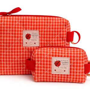 May include: Two red and white gingham cosmetic bags. The larger bag has a red bow and a red handle. The smaller bag has a wooden handle. Both bags have a label that says "Spicy Ladybug Collection".