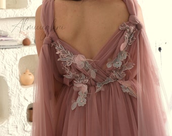 May include: A dusty rose tulle gown with a deep V-neckline and delicate floral embroidery. The gown features a flowing skirt and sheer sleeves.