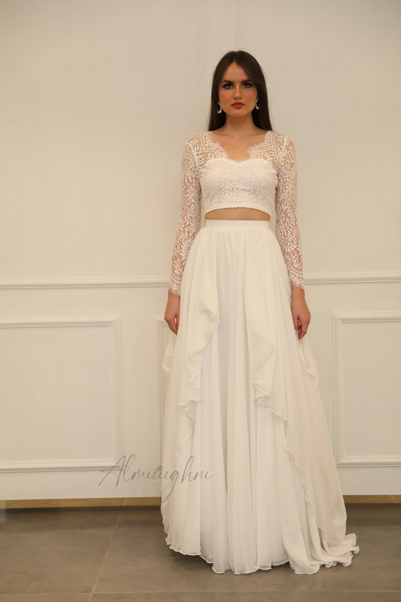 May include: A white crop top with long lace sleeves and a white flowing skirt with ruffles.