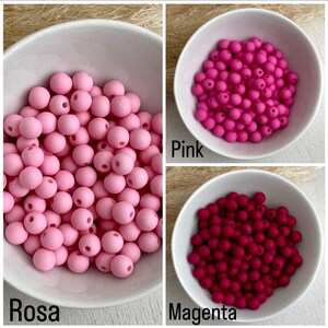Op de afbeelding: Drie kommen met ronde kralen in roze en magenta tinten. De kommen zijn gelabeld met "Rosa", "Pink" en "Magenta". De kralen hebben een matte afwerking en lijken van siliconen te zijn. Ideaal voor knutselen.