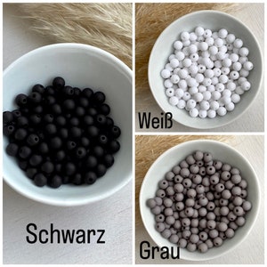 Op de afbeelding: Drie kommen met zwarte, witte en grijze kralen. De zwarte kralen zijn gemarkeerd met "Schwarz", de witte kralen met "Wei&szlig;" en de grijze kralen met "Grau". De kralen zijn klein en rond.