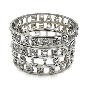 May include: Four silver bracelets stacked on top of each other. Each bracelet is made of metal and has a different name spelled out in the metal. The names are "Elizabeth", "Orange", "Alice", and "Robert".