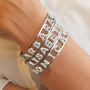 May include: Four silver bracelets with the names "SARAH", "ISABELLA", "JONICA", and "CLAIRE" spelled out in rhinestones.
