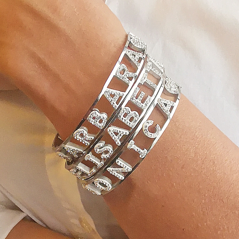 May include: Four silver bracelets with the names "SARAH", "ISABELLA", "JONICA", and "CLAIRE" spelled out in rhinestones.