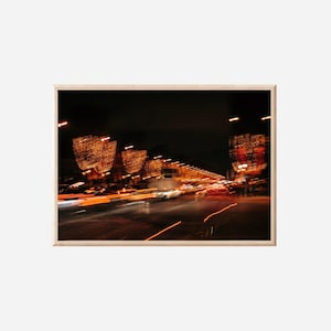 Op de afbeelding: Abstracte foto van een stadsstraat 's nachts, met vage strepen van oranje en witte lichten. De afbeelding legt de beweging van voertuigen en verlichte structuren vast, waardoor een gevoel van beweging en energie ontstaat. De donkere lucht zorgt voor een contrasterende achtergrond.