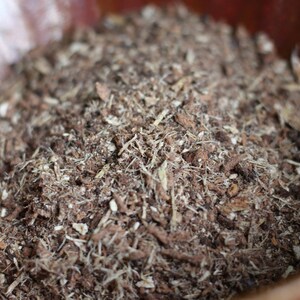 May include: Close-up of a brown and white soil mixture in a terracotta pot. The soil is made up of small pieces of bark, wood chips, and other organic matter.
