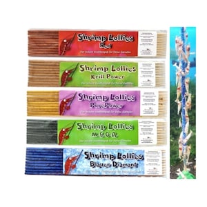 Pode incluir: Cinco pacotes de lollipops de camarão em diferentes cores e sabores: Vermelho, Krill Power, Pure Power, MEGA e Blauer Diamant. Cada pacote tem um camarão no rótulo e o texto "Shrimp Lollies" com o nome do sabor.
