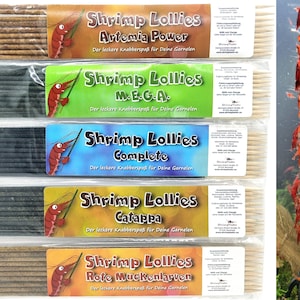 Könnte beinhalten: Fünf Packungen Shrimp Lollies, eine Art Futter für Garnelen, mit verschiedenen Geschmacksrichtungen: Artemia Power, M.E.G.A., Complete, Catappa und Rote Muckenlarven. Jede Packung hat ein buntes Etikett mit einer Garnelenillustration und dem Geschmacksnamen.