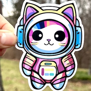 May include: A colorful sticker of a cartoon cat wearing an astronaut suit with a rainbow design. The cat has big eyes and a cute smile.