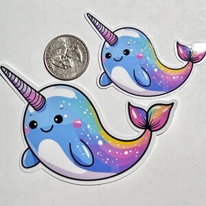 May include: Two cartoon narwhal stickers with rainbow tails and a blue and white body. The narwhals have a pink and white horn and a cute smiling face.