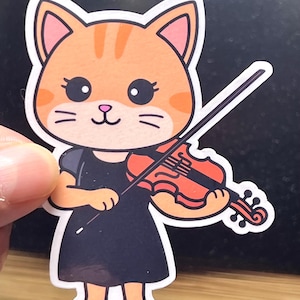 May include: A sticker featuring a cartoon cat playing a violin. The cat has orange fur with stripes, big eyes, and is wearing a black dress. The violin is orange and brown, and the bow is black.
