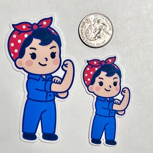 K&ouml;nnte beinhalten: Zwei Aufkleber mit einer Cartoon-Illustration von Rosie the Riveter, die ihren Bizeps anspannt. Die Aufkleber zeigen eine Frau in einem blauen Overall und einem roten Polka-Dot-Bandana. Eine M&uuml;nze liegt neben den Aufklebern zum Gr&ouml;&szlig;envergleich.