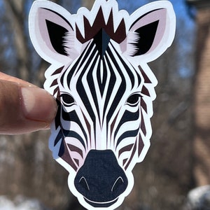 May include: A black and white zebra face sticker with a brown mane. The sticker is on a white background.