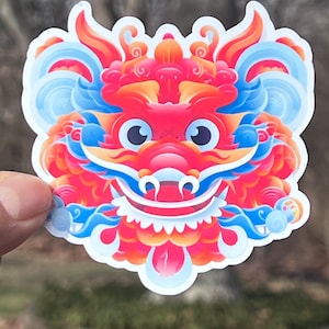 May include: A colorful sticker featuring a red, blue, and yellow dragon head with large eyes and a wide open mouth. The dragon is surrounded by swirling clouds and has a detailed design.