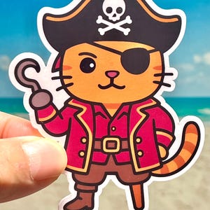 May include: A cartoon sticker of a pirate cat. The cat is orange with black stripes and wears a black pirate hat with a skull and crossbones, a red coat, and an eye patch. It holds a silver hook.