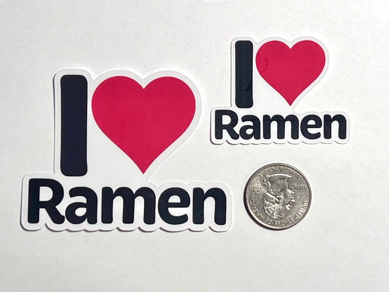 K&ouml;nnte beinhalten: Zwei Aufkleber mit dem Text "I ❤️ Ramen". Das "I" ist ein schwarzer Gro&szlig;buchstabe, das Herz ist rot und "Ramen" ist in schwarzen Buchstaben geschrieben. Eine amerikanische M&uuml;nze liegt neben den Aufklebern zum Gr&ouml;&szlig;envergleich. Die Aufkleber haben einen wei&szlig;en Rand.