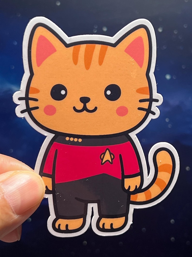 Retro sci-fi cat sticker wearing a Command Red space uniform with a black collar and gold pips. A waterproof, laminated vinyl decal shown on a professional laptop or a glass tea mug, perfect for fans of 90s space leadership and high-ranking bridge crew aesthetics.