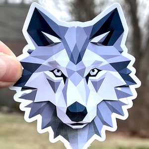 May include: A gray wolf head sticker with a geometric design. The wolf's eyes are black and the nose is dark gray.
