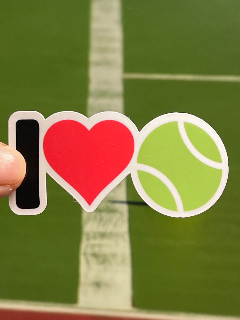 May include: A sticker with the words "I ❤️ Tennis". The "I" is black, the heart is red, and the tennis ball is green with white details. The background is a green tennis court.