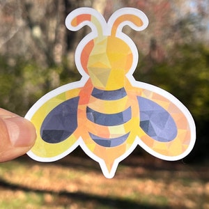 May include: A yellow and black bee sticker with a geometric design. The bee has a rounded body and two antennae.
