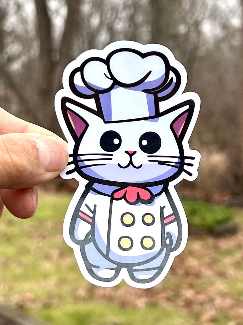 A white cat wearing a chef's hat and uniform with a red bow tie and four yellow buttons. The cat is smiling and has big black eyes. he waterproof vinyl decal features a clean white border for decorating water bottles, car windows, and laptops.