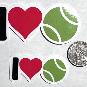 May include: Two stickers with the phrase "I love tennis." The "I" is black, the heart is red, and the tennis ball is green with white curved lines. A U.S. quarter is included for size comparison.
