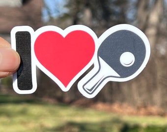 May include: A white sticker with the text "I love" followed by a red heart and a black and white table tennis paddle.
