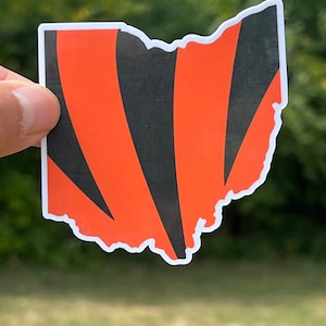 May include: A vinyl sticker of the state of Ohio with black and orange stripes, resembling the colors of a sports team.