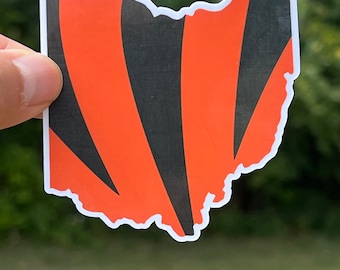 Pode incluir: Um adesivo de vinil do estado de Ohio com listras pretas e laranja, que se assemelham às cores de um time esportivo.