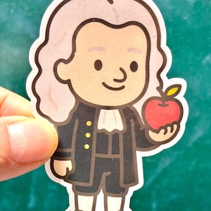 May include: A sticker featuring a cartoon illustration of Isaac Newton holding a red apple. Newton is depicted with light skin, a powdered wig, and a black coat with gold buttons. The sticker has a white border and is held against a green background.