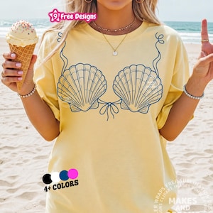 May include: A light yellow t-shirt featuring a blue seashell bra design. The shirt has the text "19 Free Designs" and "Makes and Dreams". The image also shows an ice cream cone and a hand making a peace sign. Available in 4+ colors.