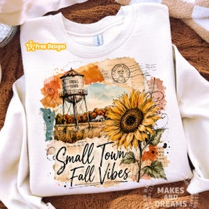May include: A cream-colored crewneck sweatshirt featuring a graphic print of a water tower labeled Small Town, a large yellow sunflower, and the text Small Town Fall Vibes. The design includes vintage-style postal stamps and watercolor textures.