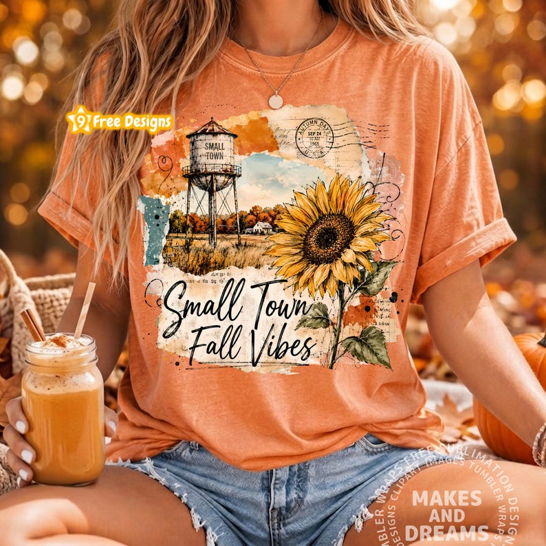 May include: An orange short-sleeve t-shirt featuring a graphic print of a water tower, a large yellow sunflower, and the text "Small Town Fall Vibes" in a cursive script. The design includes vintage-style postal stamps and textured paper elements.