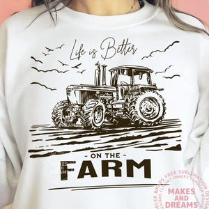 May include: White sweatshirt with a black and white tractor graphic. The design includes the text "Life is Better - ON THE - FARM" with birds and a field illustration. The sweatshirt is a casual, comfortable style.