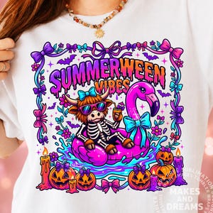 May include: White t-shirt featuring a colorful graphic with the text "SUMMERWEEN VIBES." The design includes a skeleton Highland cow wearing sunglasses and floating on a pink flamingo pool float, surrounded by pumpkins, candles, and bows.