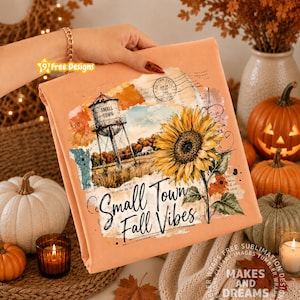 May include: A peach-colored fabric featuring a graphic print of a water tower, a large yellow sunflower, and the text Small Town Fall Vibes. The design includes vintage-style paper textures, ink splatters, and a circular postmark stamp.