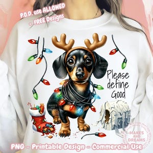 Op de afbeelding: Een witte sweatshirt met een teckel met rendiergeweien en kerstverlichting. De hond is omringd door een kerstsok, een kaars en de tekst "Please define Good". Het ontwerp is een printbaar PNG.