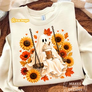 May include: A cream-colored crewneck sweatshirt featuring a graphic of a white ghost sitting on a swing, holding a cup labeled Pumpkin Spice Latte. The design is surrounded by yellow sunflowers, orange poppies, and autumn leaves with small hearts.