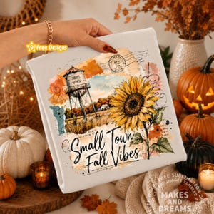 May include: A white sweatshirt featuring a graphic print of a water tower labeled 'Small Town', a large yellow sunflower, and the text 'Small Town Fall Vibes' in black script. The design includes watercolor-style orange and blue accents.